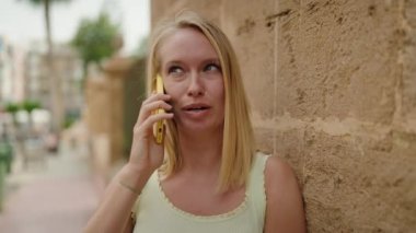 Genç sarışın kadın gülümsüyor. Kendine güveni tam. Akıllı telefondan konuşuyor.