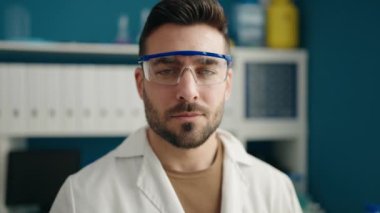 Young hispanic man wearing scientist uniform standing with arms crossed gesture at laboratory