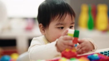 Adorable hispanic baby playing with construction blocks sitting on table at kindergarten