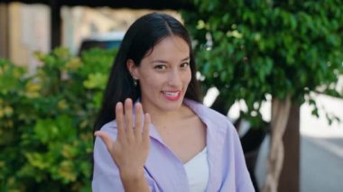 Genç, güzel İspanyol kadın gülümsüyor kendinden emin bir şekilde sokakta el kol geziyor.