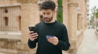 Sokakta akıllı telefon ve kredi kartı kullanan genç bir Arap.