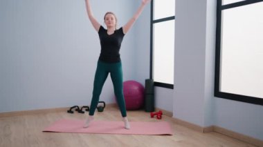 Genç sarışın kadın spor merkezinde atlarken kendinden emin bir şekilde gülümsüyor.