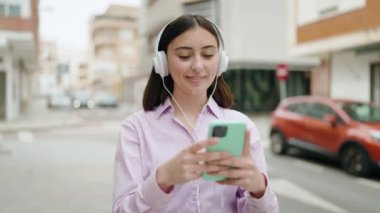 Genç İspanyol kadın sokakta müzik dinlerken kendinden emin gülümsüyor.