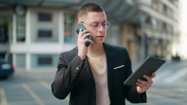 Latin kökenli genç bir yönetici, akıllı telefondan konuşuyor. Sokakta dokunmatik ped kullanıyor.