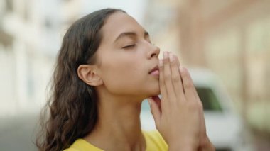 Young african american woman praying with closed eyes at street