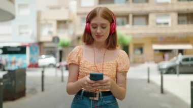 Genç, kızıl saçlı, kendine güvenen, sokakta yürürken müzik dinleyen bir kadın.