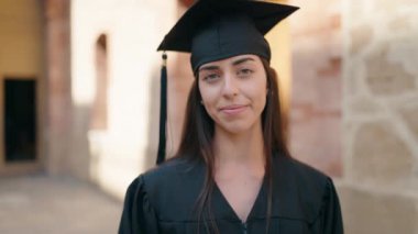 Mezuniyet üniforması giyen genç İspanyol kadın üniversiteyi parmağıyla işaret ediyor.