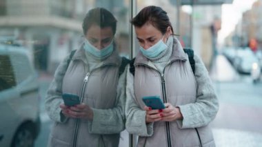 Sokaklarda akıllı telefon kullanan orta yaşlı kadın tıbbi maske takıyor.