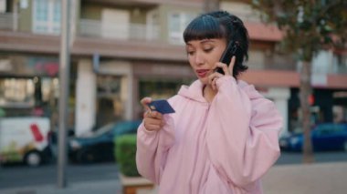 Genç İspanyol kadın akıllı telefondan konuşuyor ve sokakta kredi kartı kullanıyor.