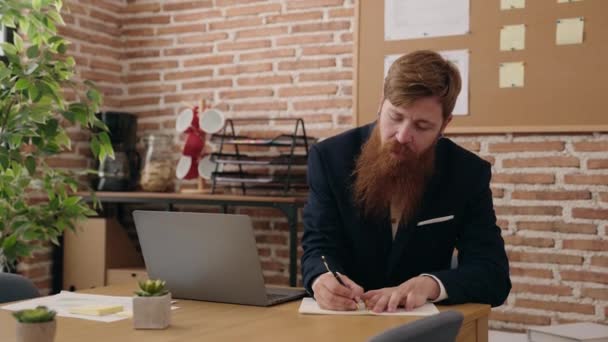 Młody Rudowłosy Człowiek Biznes Pracownik Pomocą Laptopa Pisanie Notatniku Biurze — Wideo stockowe