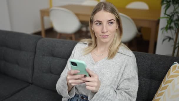 Mujer Rubia Joven Usando Teléfono Inteligente Sentado Sofá Casa — Vídeos de Stock