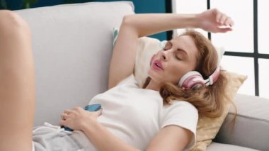 Genç, güzel İspanyol kadın evdeki kanepede rahatça müzik dinliyor.