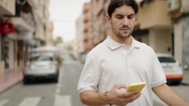 Genç İspanyol adam sokakta akıllı telefon kullanıyor.