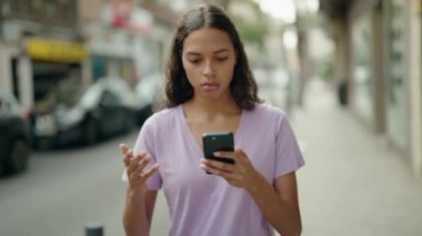 Genç Afrikalı Amerikalı kadın sokakta endişeli bir ifadeyle akıllı telefon kullanıyor.
