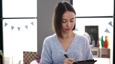 Young beautiful hispanic woman working as a teacher using touchpad at kindergarten