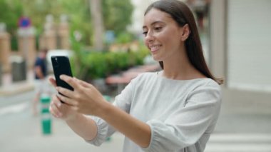 Genç ve güzel İspanyol kadın gülümsüyor. Kendine güveni tam. Sokakta akıllı telefonun yanında selfie çekiyor.