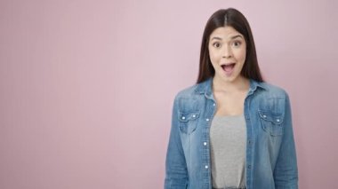 Genç, güzel, İspanyol bir kadın gülümsüyor. Kendine güveni tam, pembe arka planda, parmaklarını yana doğru gösteriyor.