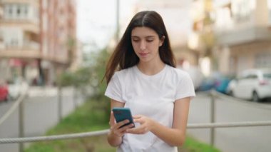 Genç İspanyol kız gülümsüyor. Kendine güveni tam. Sokakta akıllı telefonun yanında özçekim yapıyor.