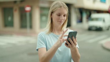 Sokakta akıllı telefon kullanan, kendine güvenen genç sarışın kadın.