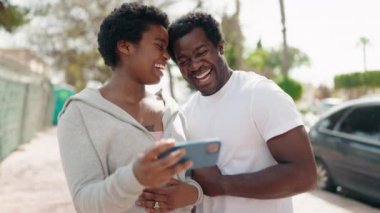 Afro-Amerikalı erkek ve kadın çift sokakta akıllı telefondan video izliyor.