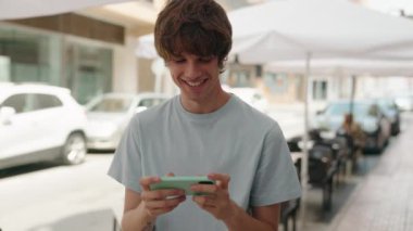 Sarışın genç adam gülümsüyor. Akıllı telefondan izliyor.