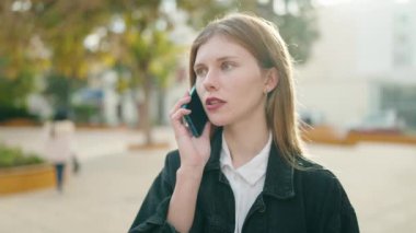 Beyaz bir kadın akıllı telefondan konuşuyor ve parkı gözetliyor.