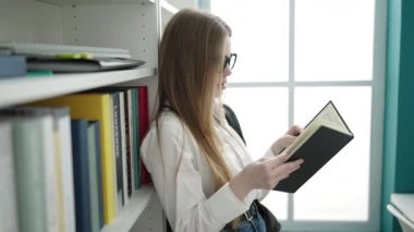 Young blonde woman student standing reading book at university classroom