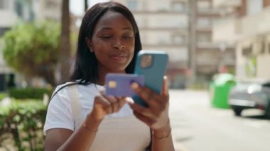 Young african american woman using smartphone and credit card at park