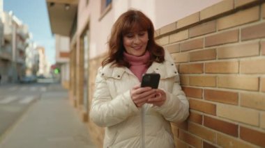 Middle age redhead woman smiling confident using smartphone at street