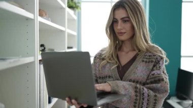 Young blonde woman teacher using laptop standing at library university