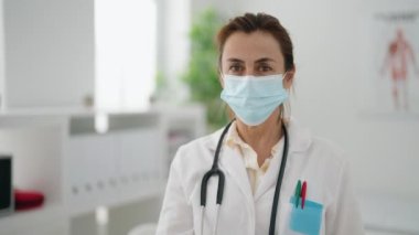 Klinikte termometre tutan doktor üniforması giyen orta yaşlı bir kadın.