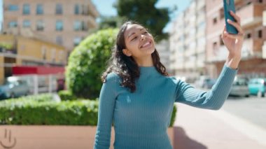 Genç Afrikalı Amerikalı kadın gülümsüyor. Kendine güveni tam. Sokakta akıllı telefondan selfie çekiyor.