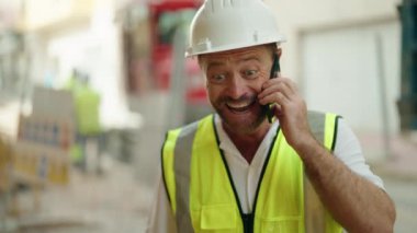 Orta yaşlı mimar akıllı telefondan konuşuyor. Sokakta kazanan yüz ifadesi var.