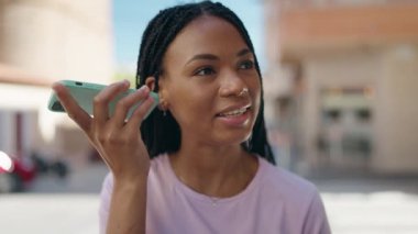 Afro-Amerikalı kadın gülümsüyor. Caddedeki akıllı telefondan kendine güvenen sesli mesaj dinliyor.
