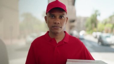 Young latin man delivery worker holding package doig ok gesture with finger at street