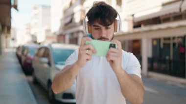 Young hispanic man smiling confident playing video game at street