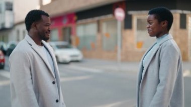 Afroamerikan çift sokakta el ele tutuşup gülümsüyor.