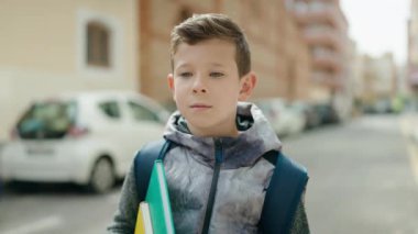 Sarışın çocuk elinde kitaplarla caddede duruyor.