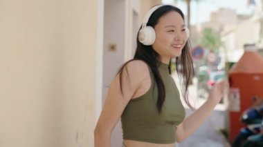 Young chinese woman listening to music and dancing at street