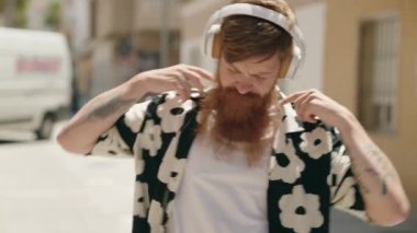 Young redhead man listening to music and dancing at street