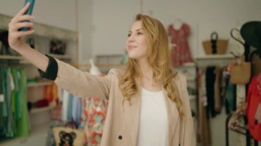 Genç sarışın müşteri giyim mağazasında akıllı telefon ile selfie çekiyor.