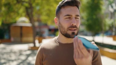 Genç İspanyol adam gülümsüyor. Parktaki akıllı telefondan konuşuyor.