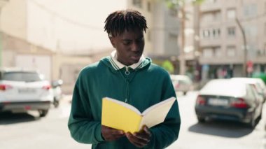 Afro-amerikan adam rahat bir ifadeyle sokakta kitap okuyor.