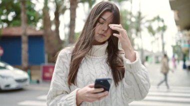 Genç, güzel, İspanyol bir kadın sokakta akıllı telefon kullanarak gülümsüyor.