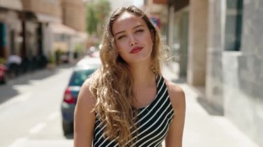 Young beautiful hispanic woman smiling confident doing ok sign with thumbs up at street