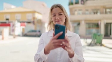 Young blonde woman making picture by the smartphone at street