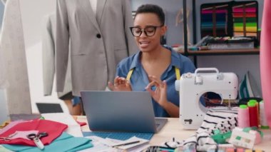 Afro-Amerikalı kadın terzi terzide video görüşmesi yapıyor.