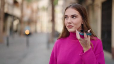 Young blonde woman smiling confident listening audio message by the smartphone at street