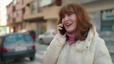 Middle age redhead woman smiling confident talking on the smartphone at street