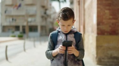 Sarışın çocuk sokakta akıllı telefon kullanıyor.